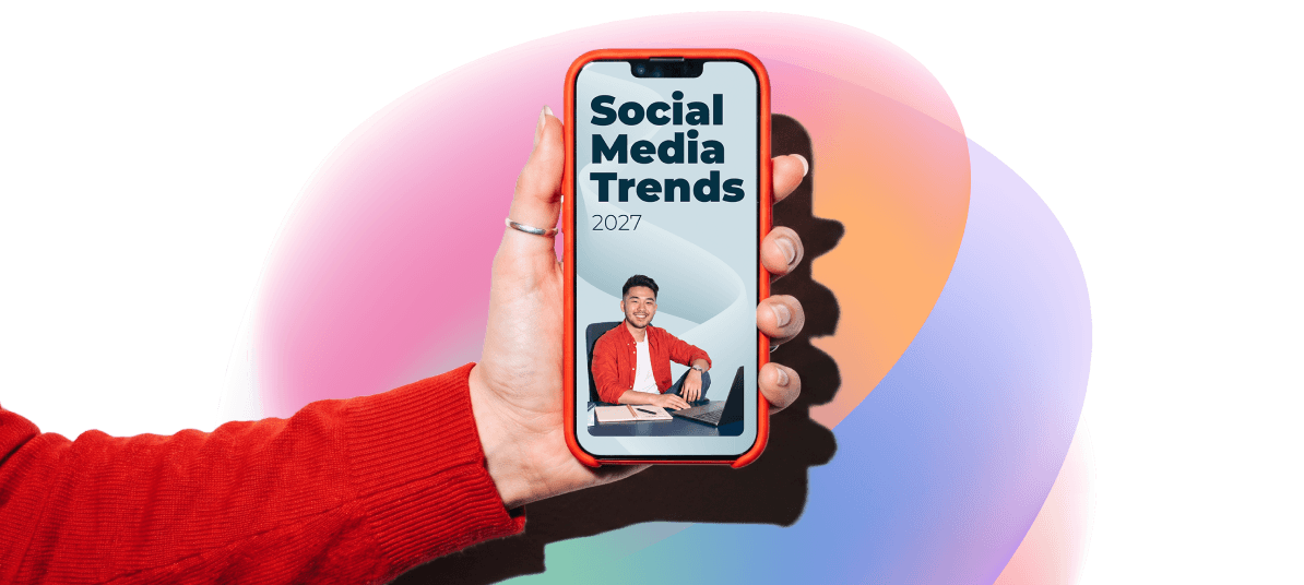 A hand in a red sleeve holds a phone displaying "Social Media Trends 2027" with a smiling man at a desk.